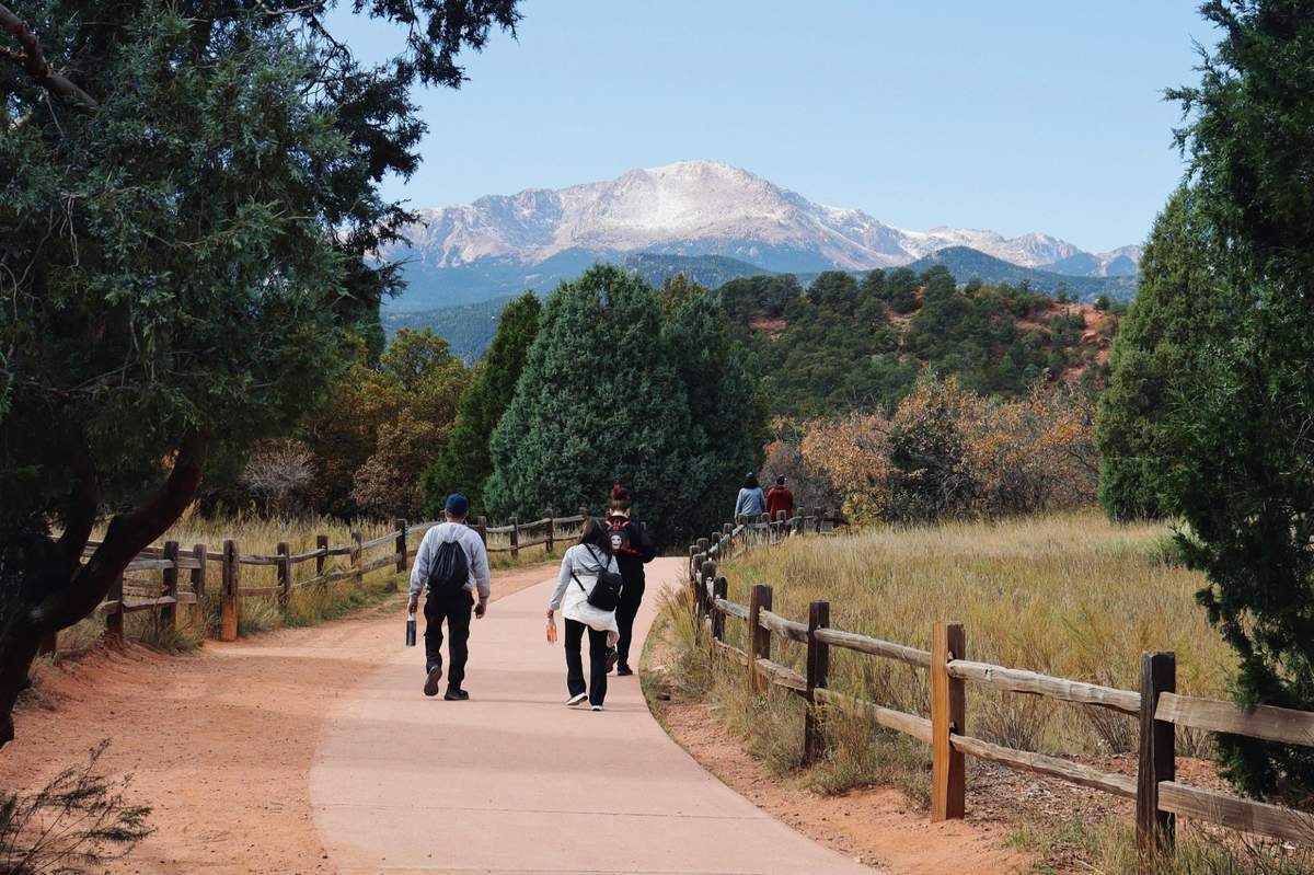 People walking a trail with Pikes Peak in the background